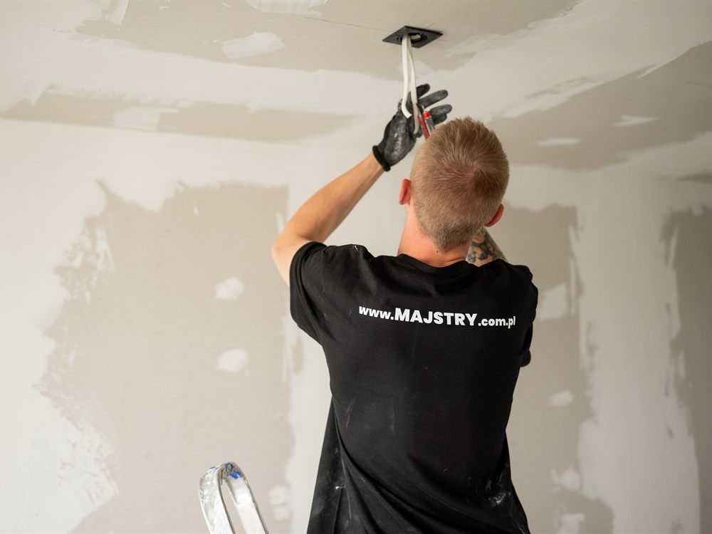 Instalator montuje puszkę podtynkową w suficie z płyty gipsowo-kartonowej